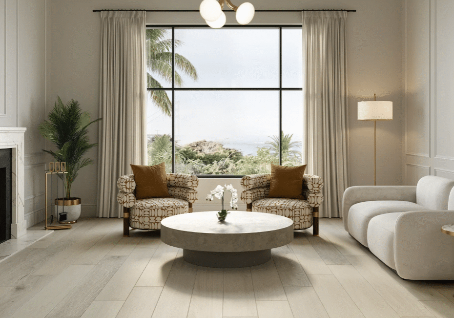 Modern living room with a marble fireplace, two patterned armchairs, a white sofa, a round coffee table, potted plants, and large window showing palm trees and sky. Neutral tones and gold accents decorate the space.